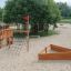 Kinderspielplatz aus Holz mit Rutsche und Sandkasten in einem Park.