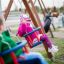 Kinder auf Schaukelsitzen auf einem Spielplatz, Mädchen in rosa Kleidung.